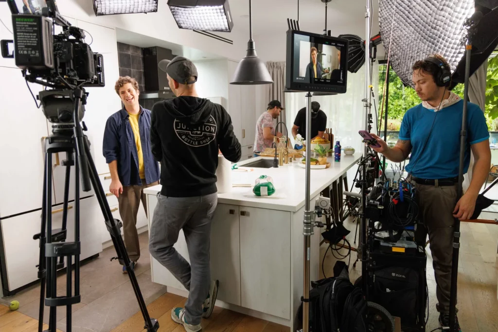 A crew filming in a kitchen set, camera on sticks