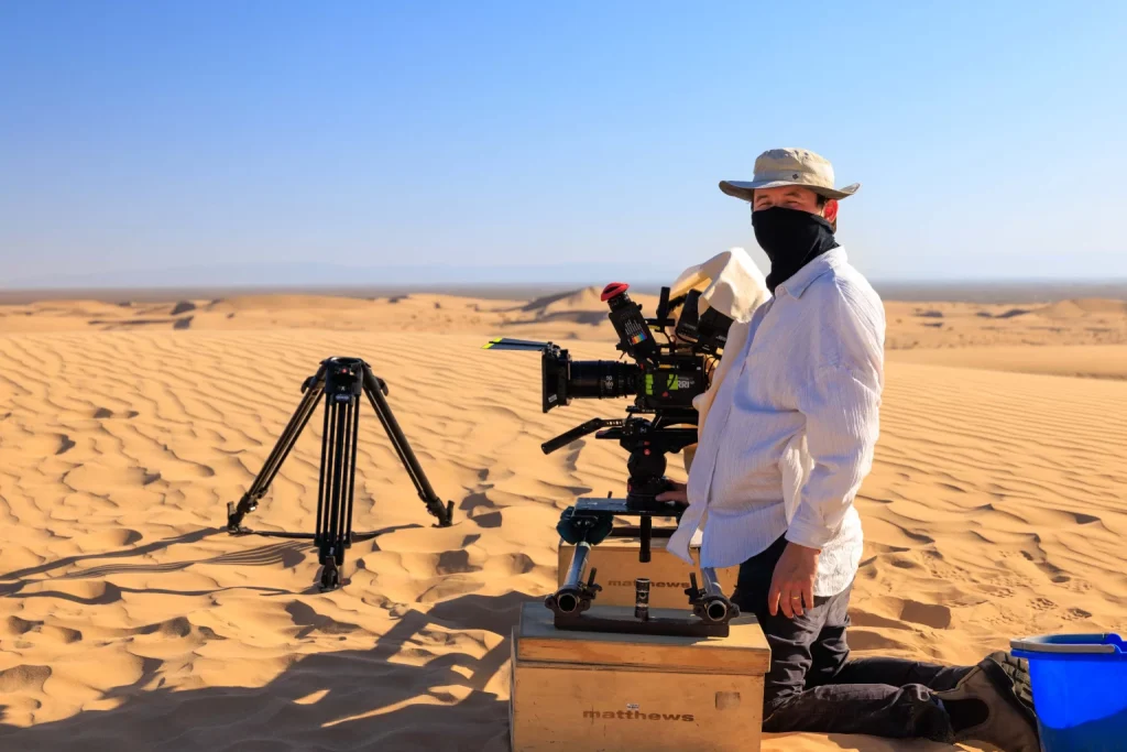 A filmmaker with a cinema camera on a tripod in the desert dunes