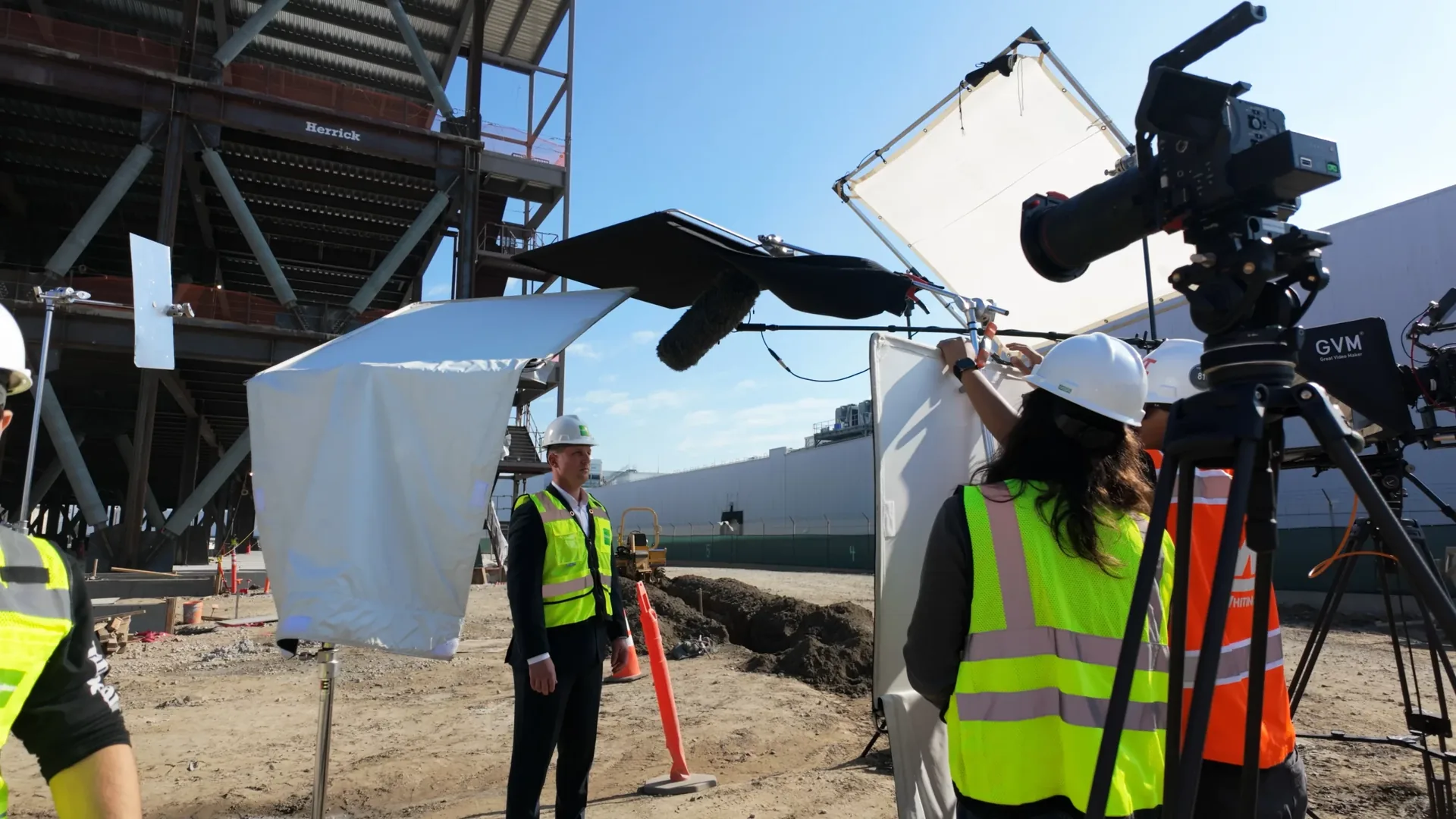 A camera crew filming workers in hi-vis vests on a construction site